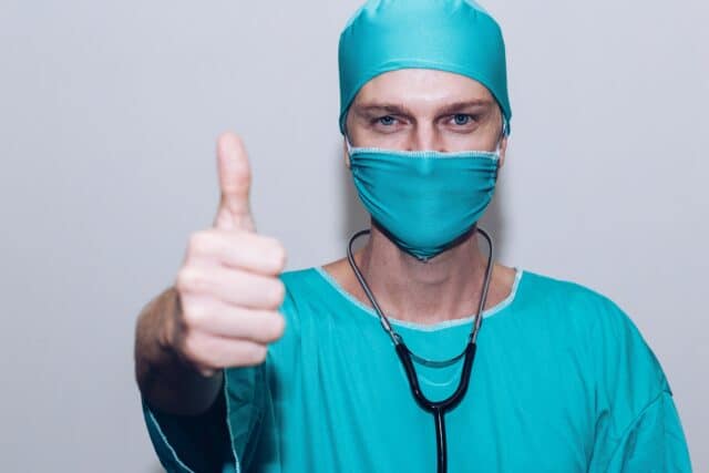 man with thumb up in green operating gown