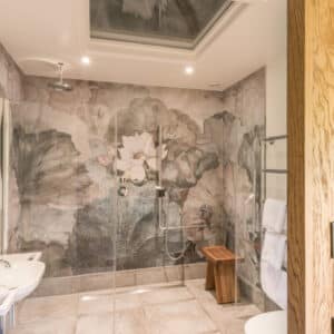 White sink against beige wall and shower with silver bars and grey/black wall mural