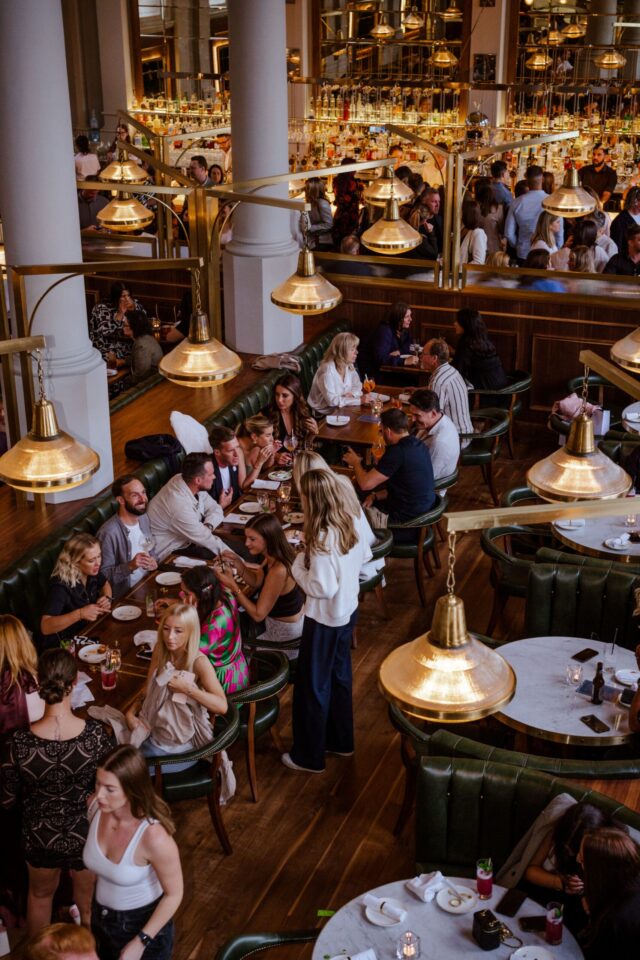 Restaurant with many people sitting at brown tables with white lights and brown wood floor